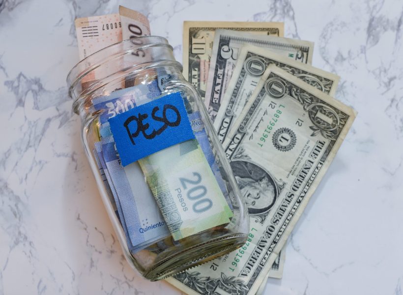 A high angle view of pesos in a jar with a blue [pesos] sticker on it on the table near dollars