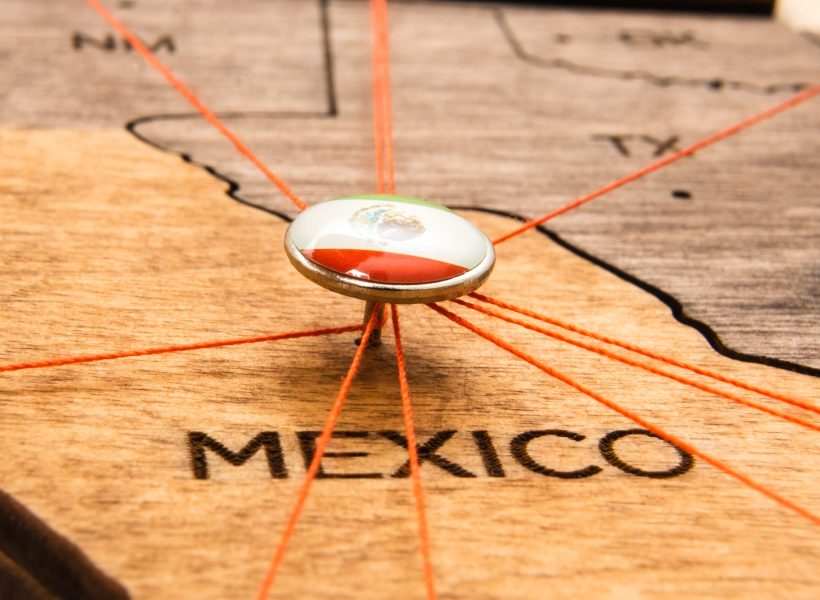 Mexico flag on the pushpin and red threads on the wooden map. Travel or logistic routes. Influence in geopolitics and world economy.